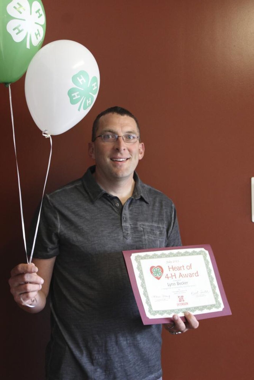 Lynn Becker holding 4-H balloons and a certificate. 