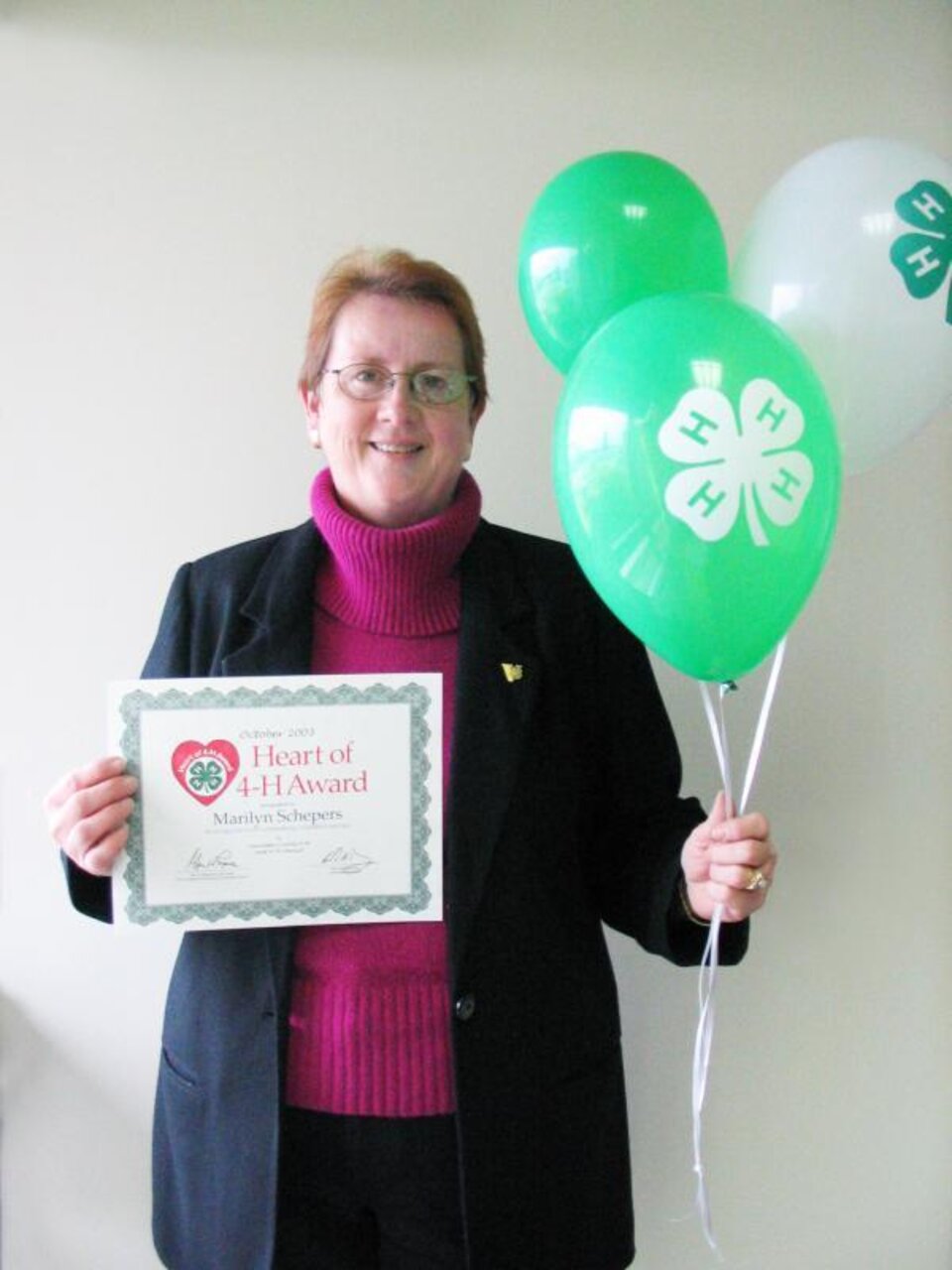 Marilyn Schepers holding balloons and a certificate. 