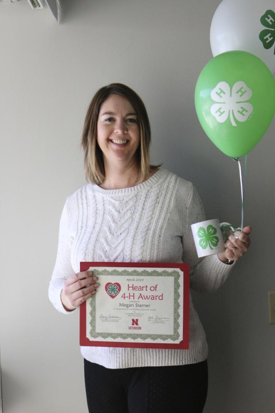 Megan Starner holding 4-H balloons, a 4-H mug, and a certificate. 