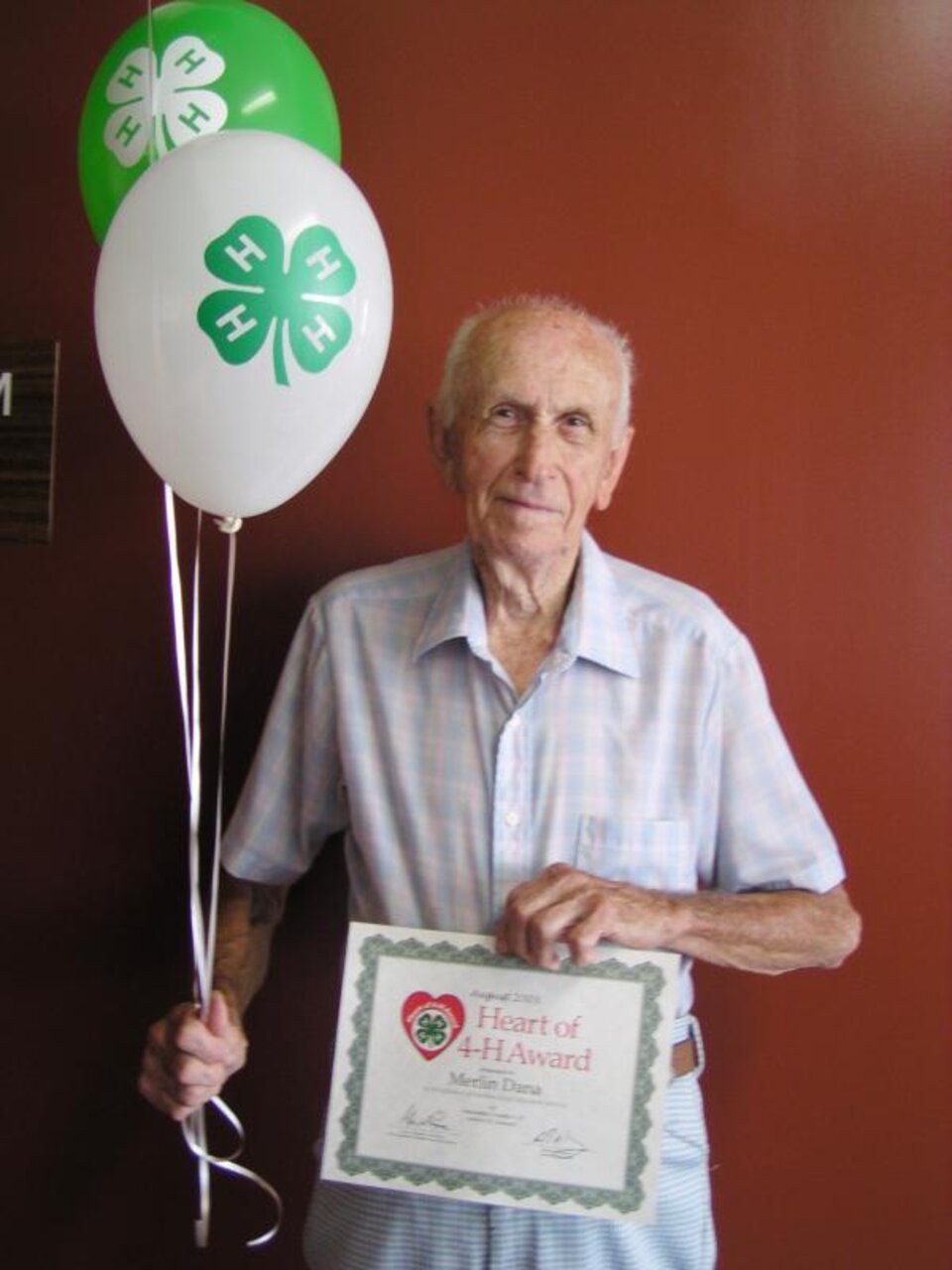 Merlin Dana holding balloons and a certificate. 