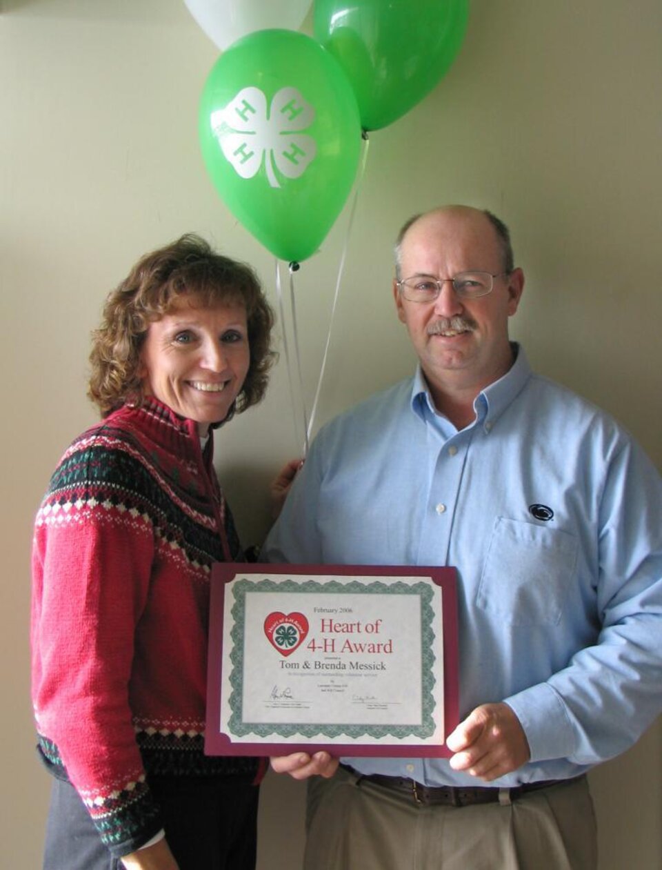 Tom and Brenda Messick standing together holding balloons and a certificate 