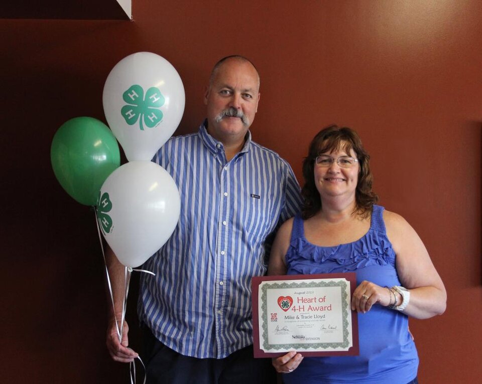 Mike & Tracie Lloyd standing together and holding 4-H balloons and a certificate. 