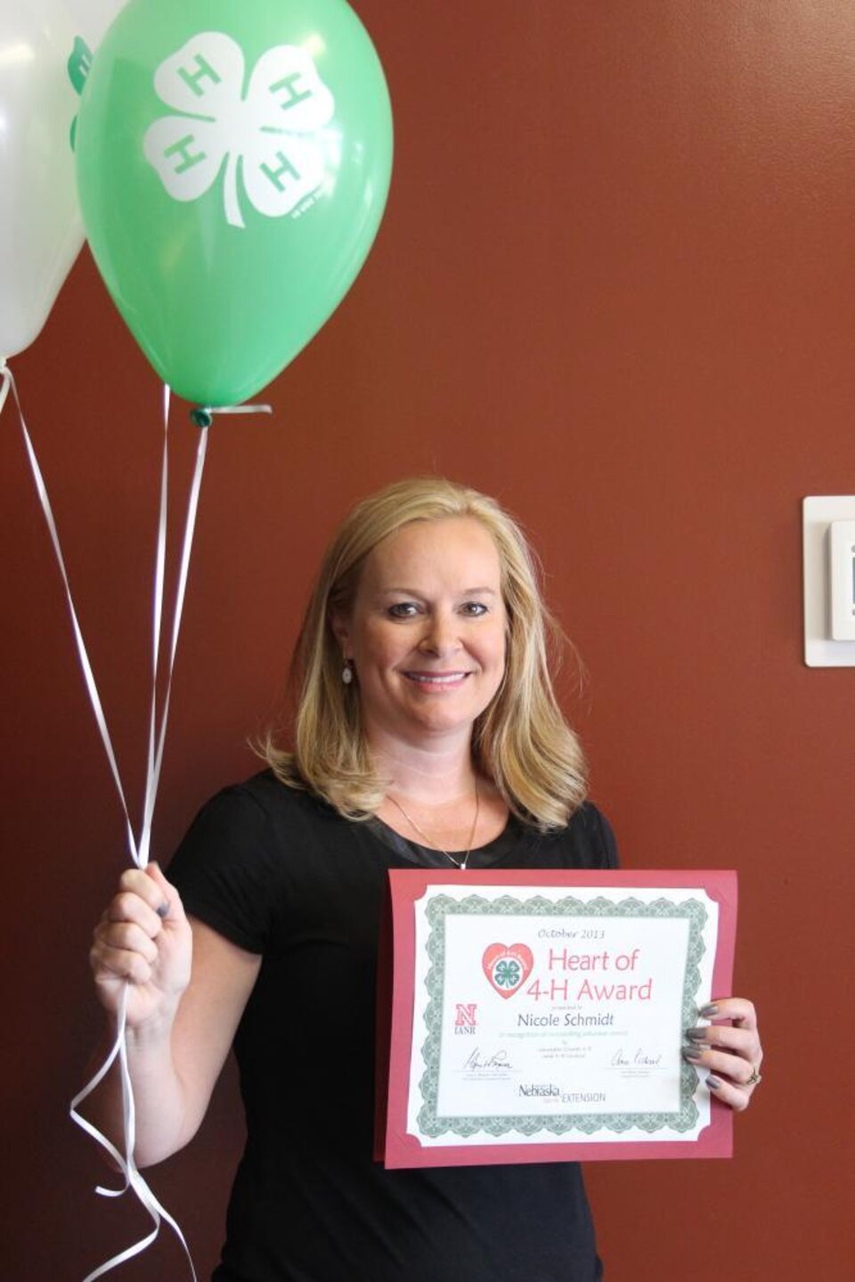 Nicole Schmidt holding 4-H balloons and a certificate. 