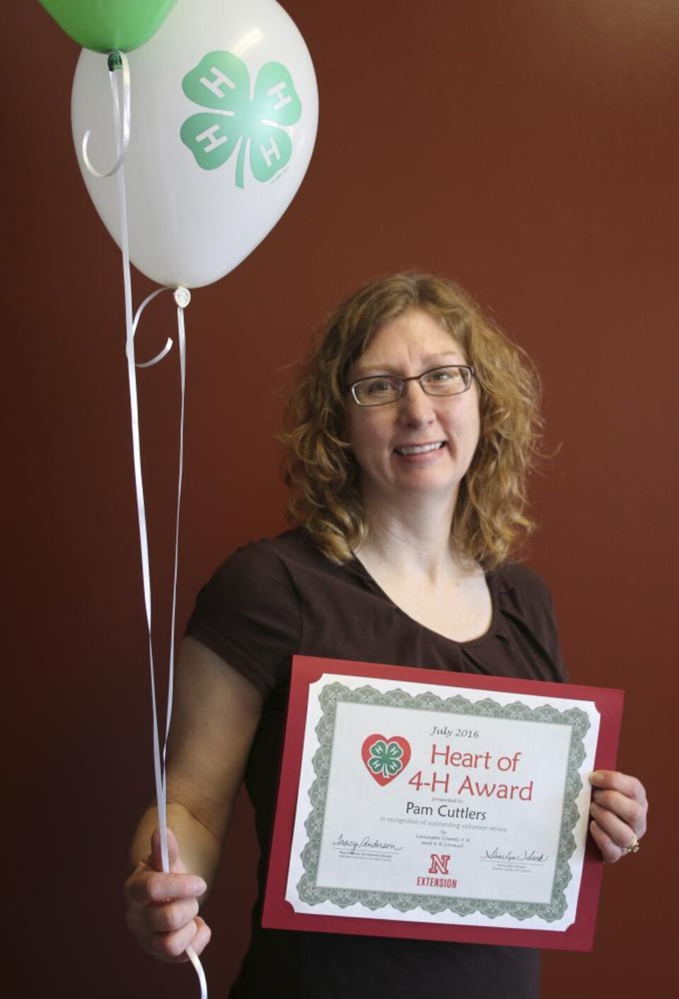 Pamela Cuttlers holding 4-H balloons and a certificate. 