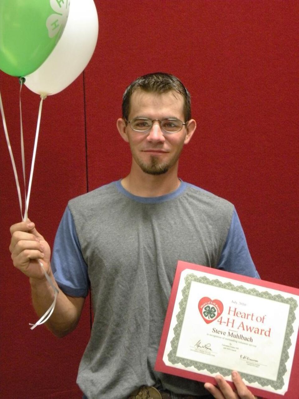 Steve Muhlbach holding 4-H balloons and a certificate. 