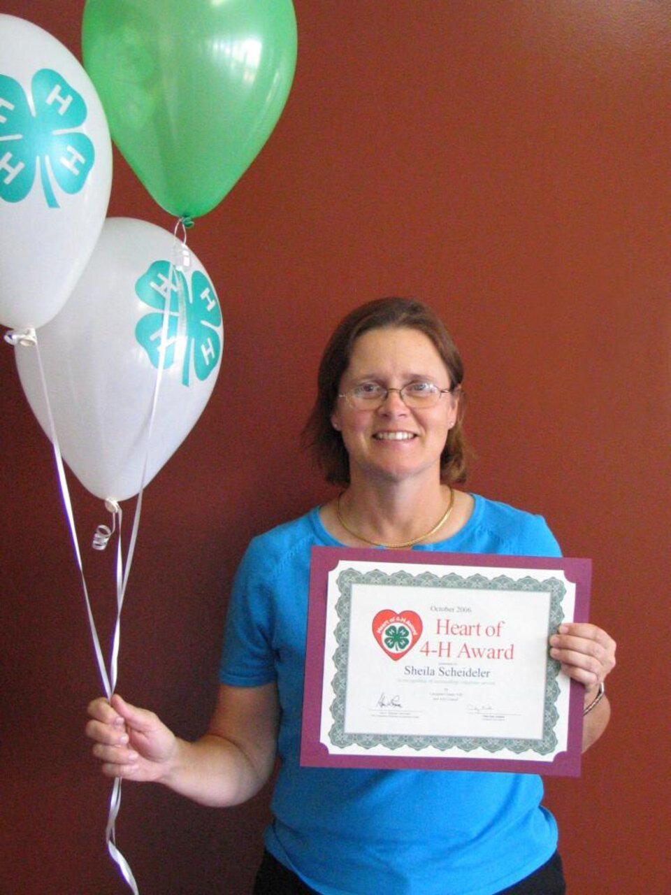 Sheila Scheideler holding balloons and a certificate 