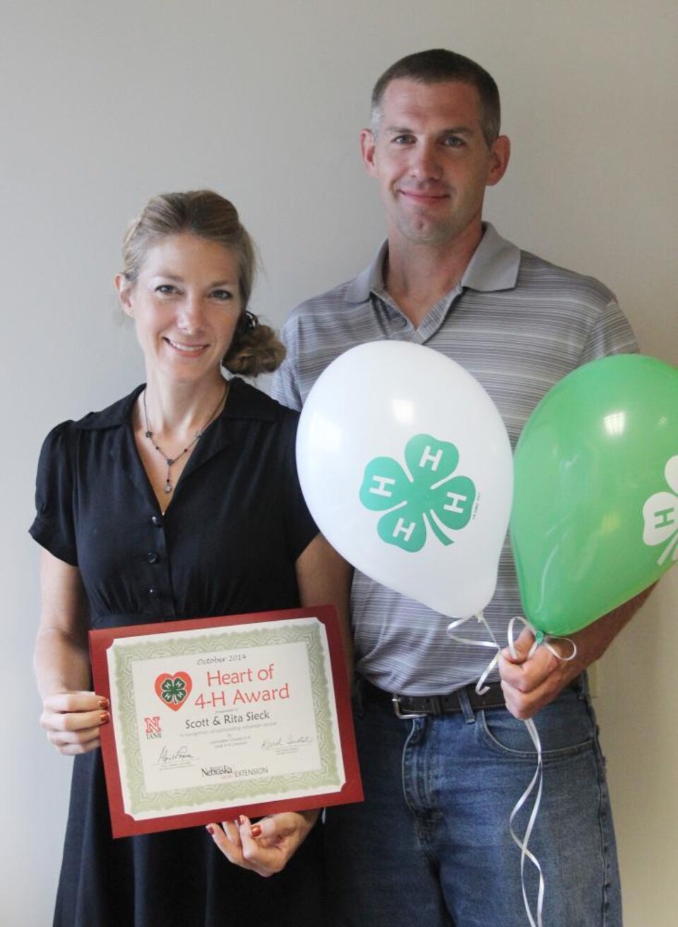 Scott and Rita Sieck standing together and holding 4-H balloons and a certificate. 