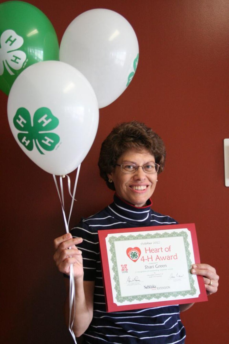 Shari Green holding 4-H balloons and a certificate. 