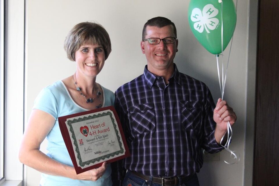 Steward & Kris Spath standing together and holding 4-H balloons and a certificate. 