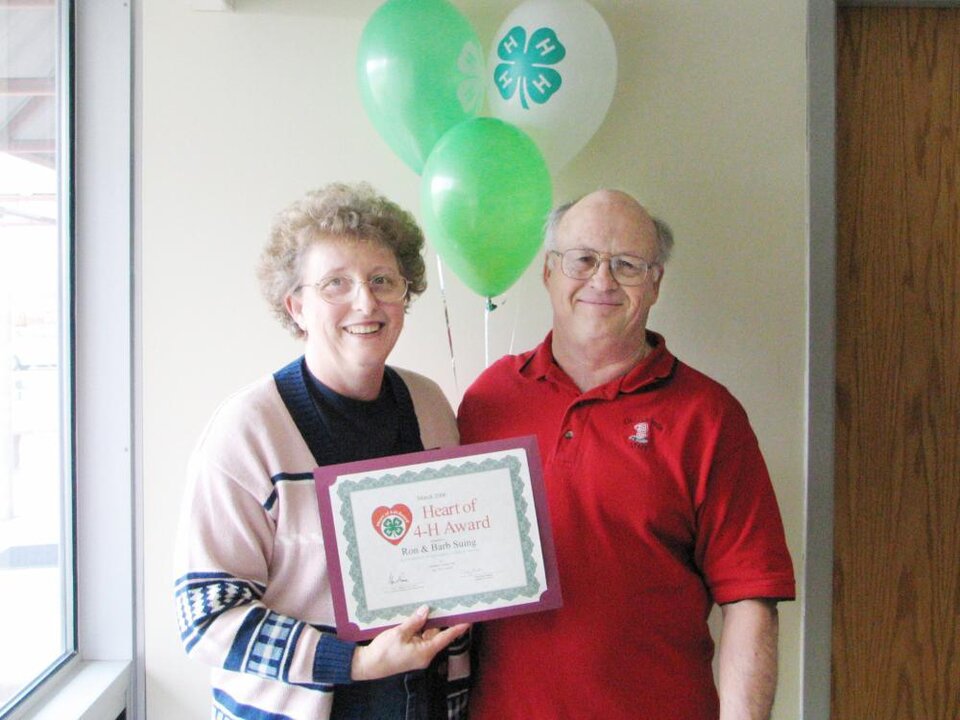 Barb and Ron Suing standing together holding balloons and a certificate 