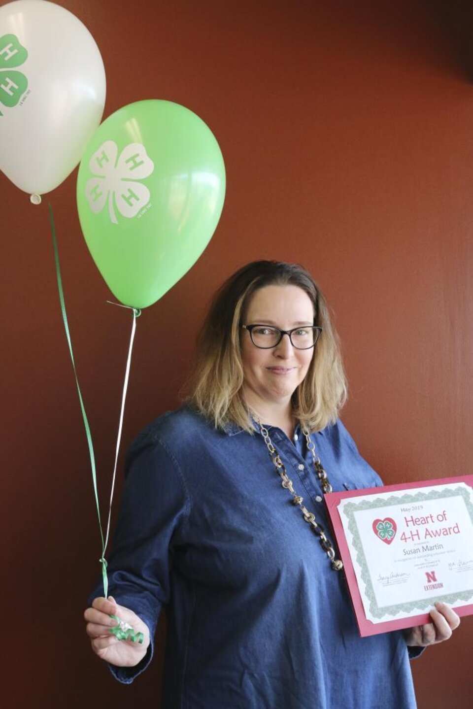 Susan Martin holding 4-H balloons, a 4-H mug, and a certificate. 