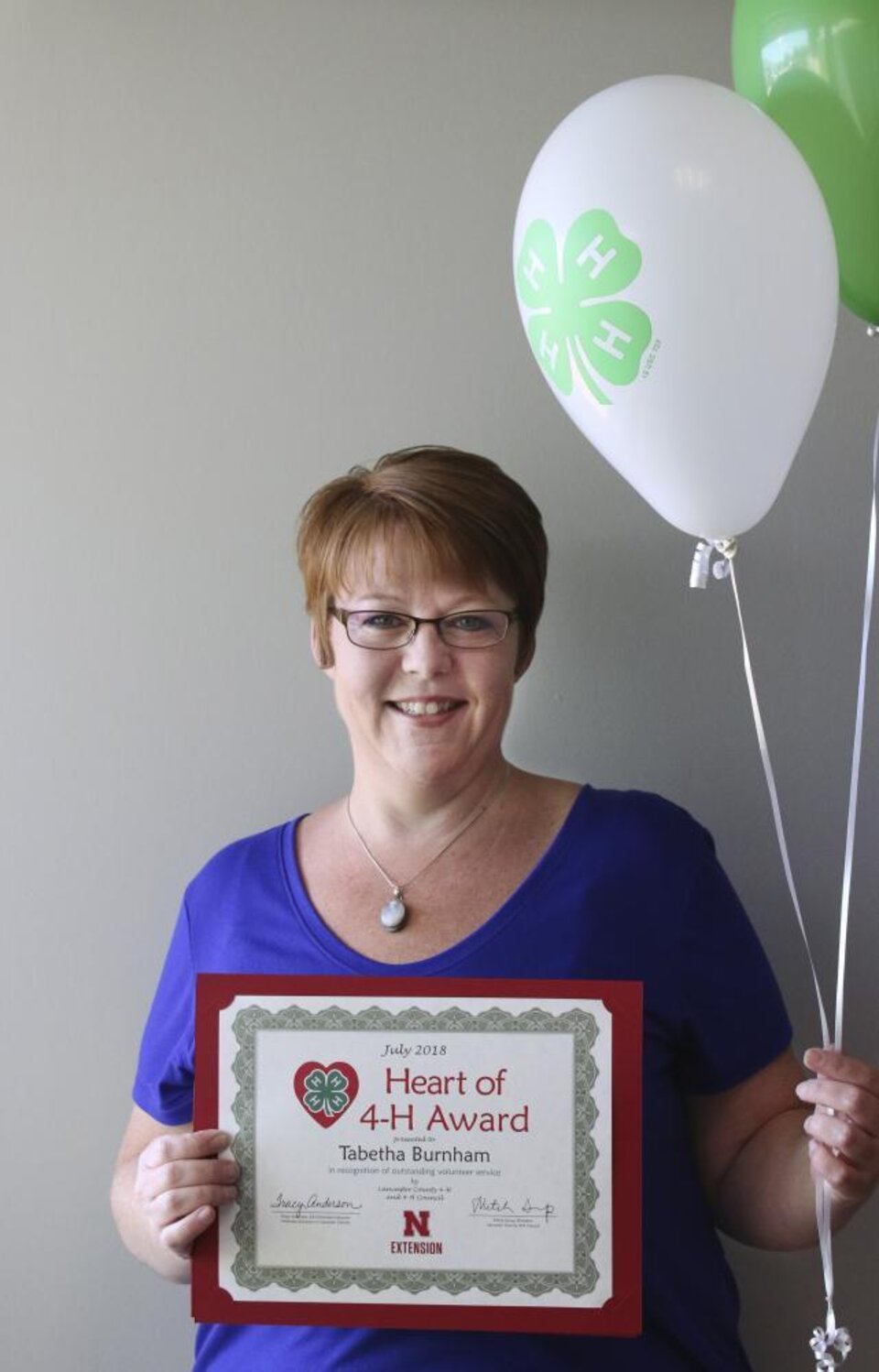 Tabetha Burnham holding 4-H balloons and a certificate. 