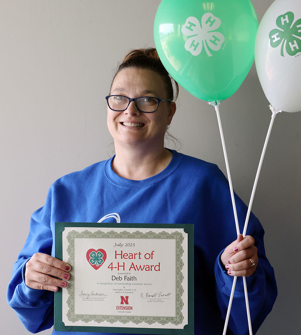 A smiling woman holding two balloons with 4-H logos and a certificate that says Heart of 4-H