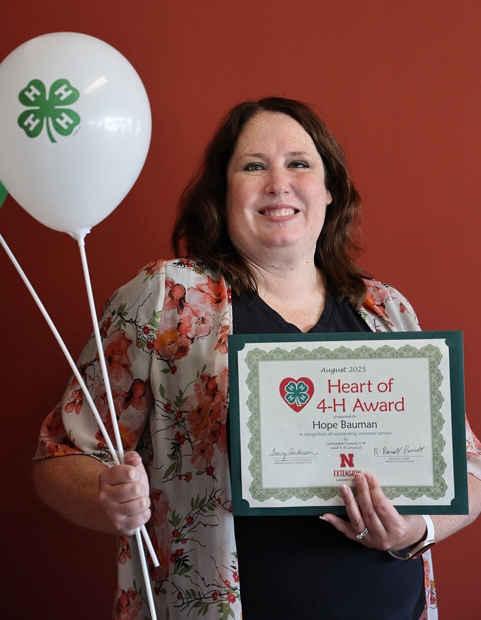 A smiling woman holding two balloons with 4-H logos and a certificate that says Heart of 4-H