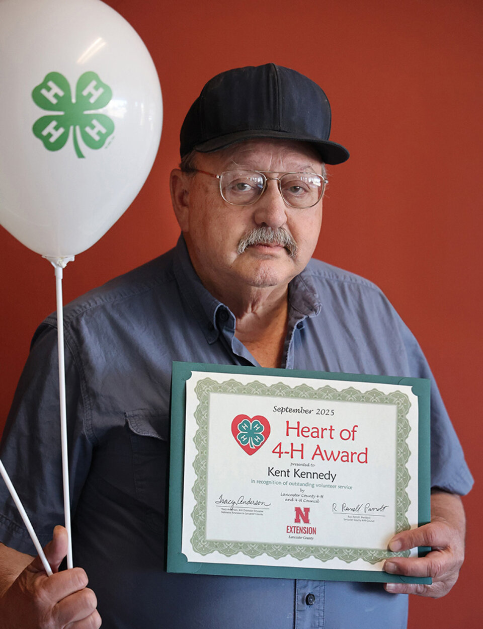 A man holding two balloons with 4-H logos and a certificate that says Heart of 4-H