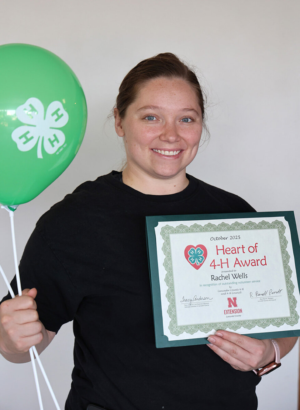 Rachel Wells A smiling woman holding two balloons with 4-H logos and a certificate that says Heart of 4-H