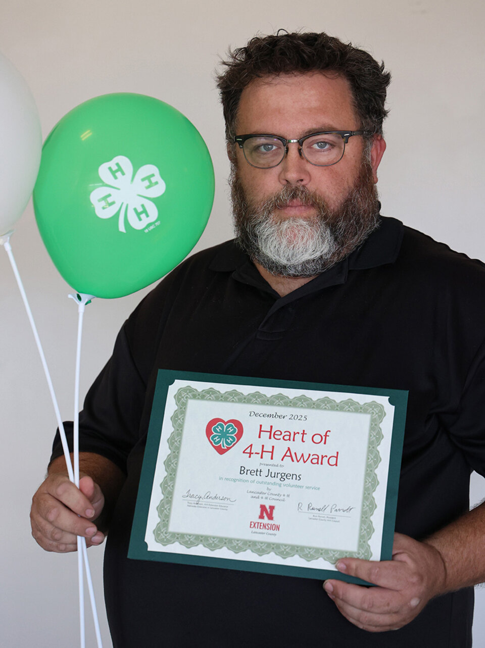 Brett Jurgens A man holding two balloons with 4-H logos and a certificate that says Heart of 4-H