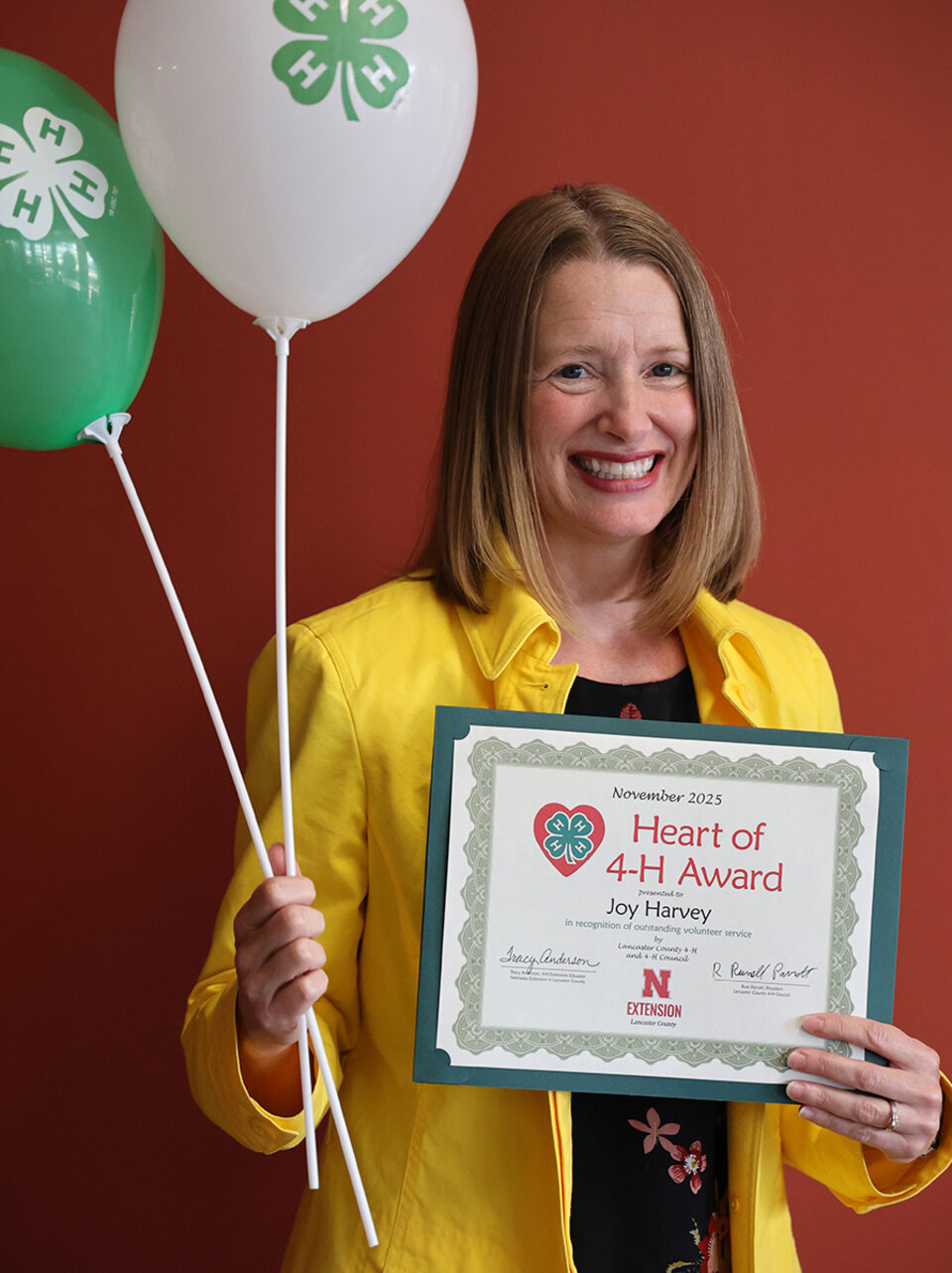 Joy Harvey A smiling woman holding two balloons with 4-H logos and a certificate that says Heart of 4-H