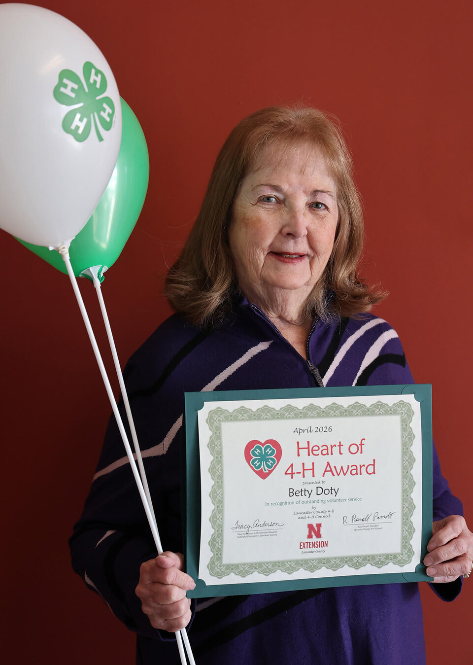 A smiling woman holding two balloons with 4-H logos and a certificate that says Heart of 4-H