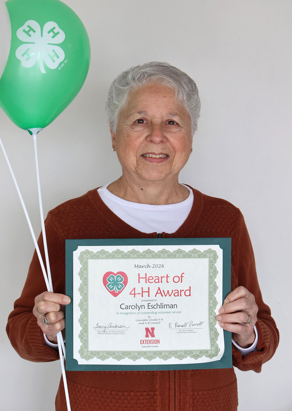 A smiling woman holding two balloons with 4-H logos and a certificate that says Heart of 4-H