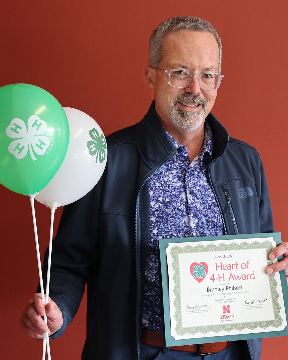 Brad Philson holding 4-H balloons and a Heart of 4-H Award certificate