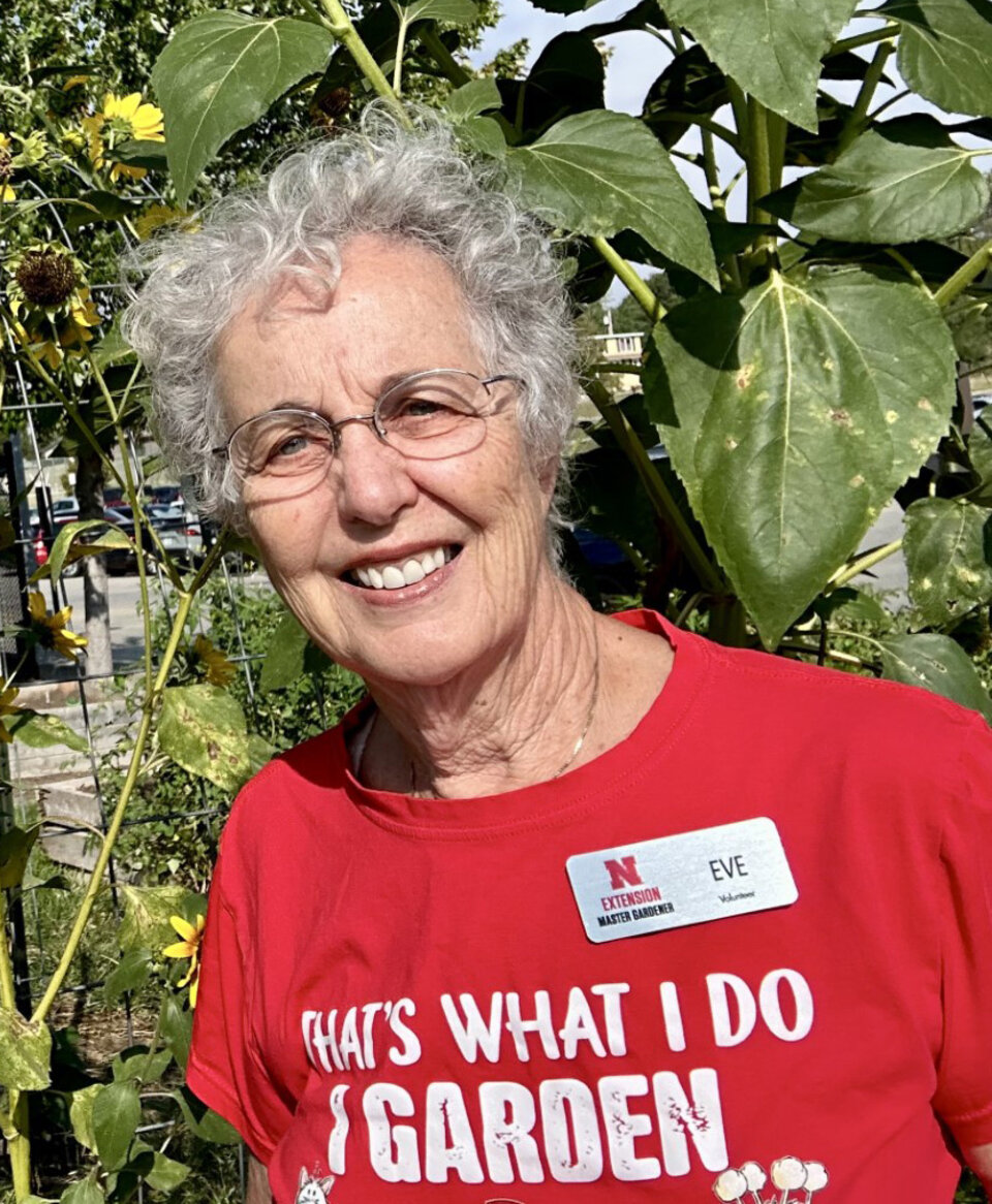 Eve Hoffman wearing a red gardening shirt surrounded by tall sunflowers