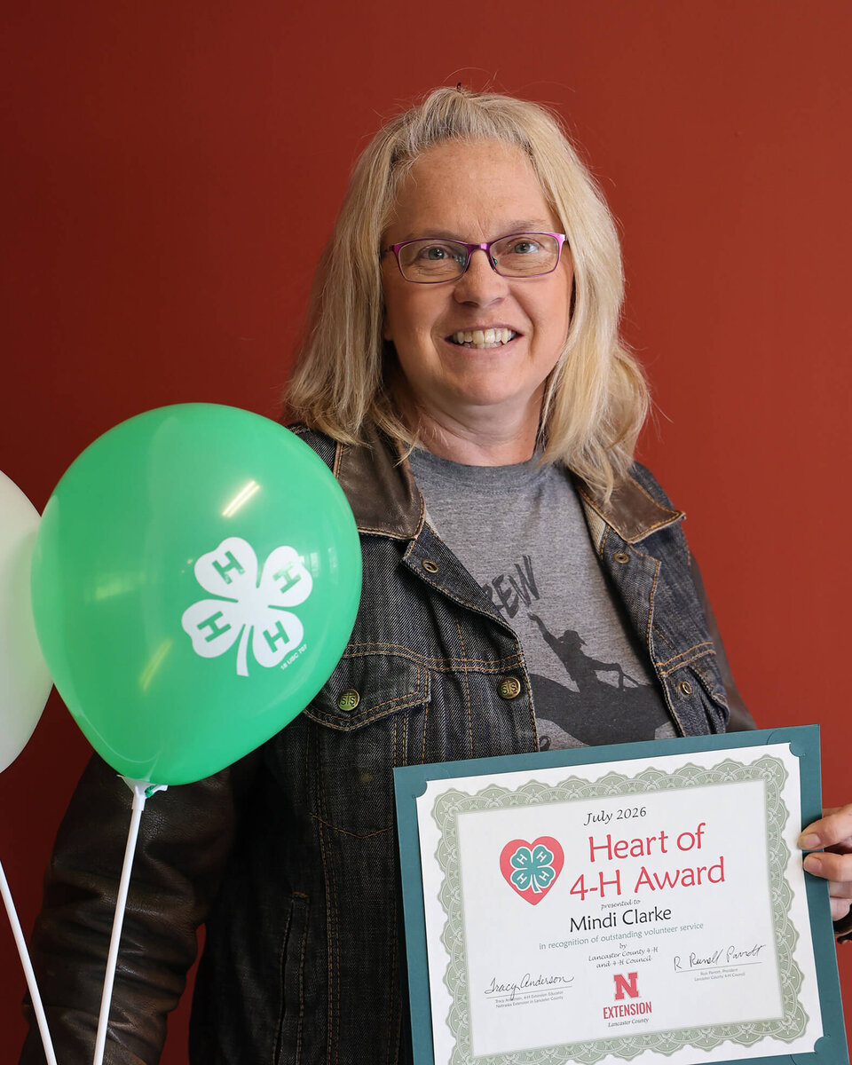 Heart of 4-H Award certificate held beside green and white balloons, red background.